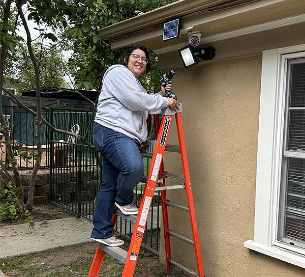 BOOST student Abby Installing solar security project on ladder