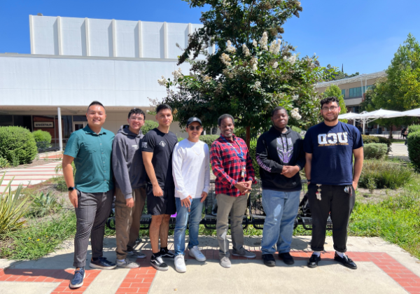 A group of men smiling in front of a white building.