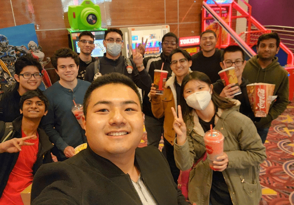 A group of men and women smiling in front of bright video games in a theater.