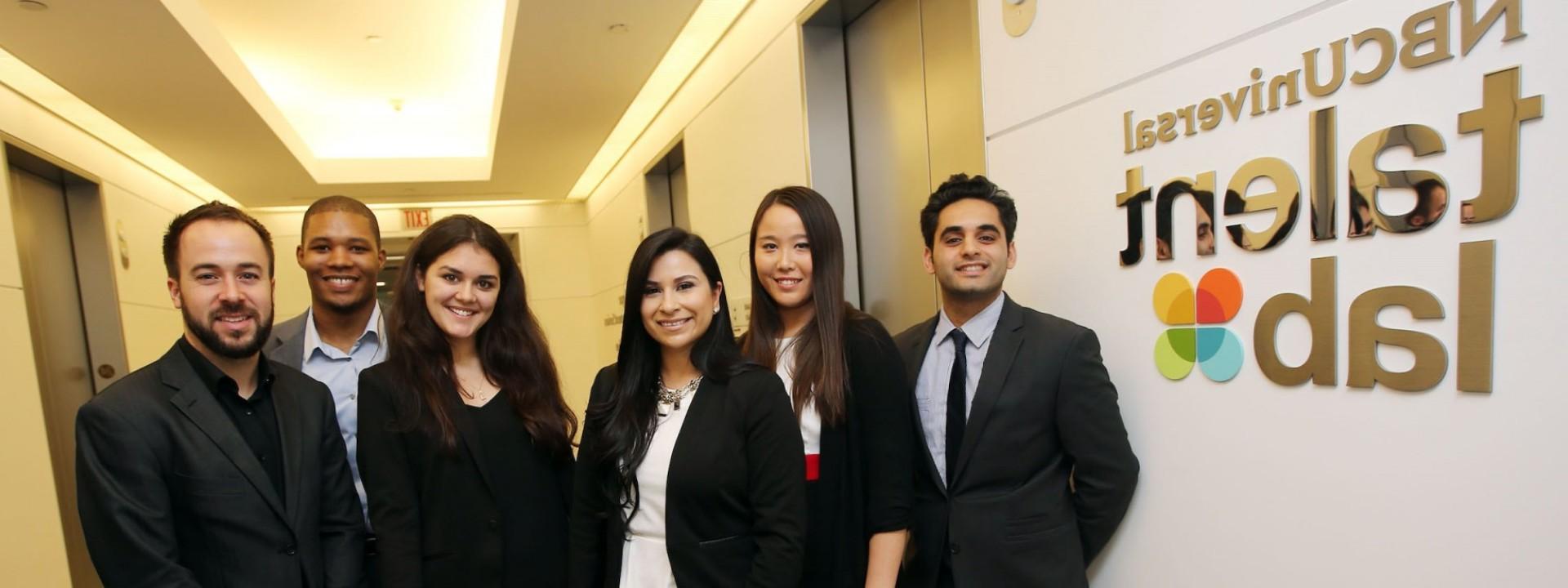 Group of Cal State LA students in business attire standing grouped in front of the NBC Universal Talent Lab sign. 